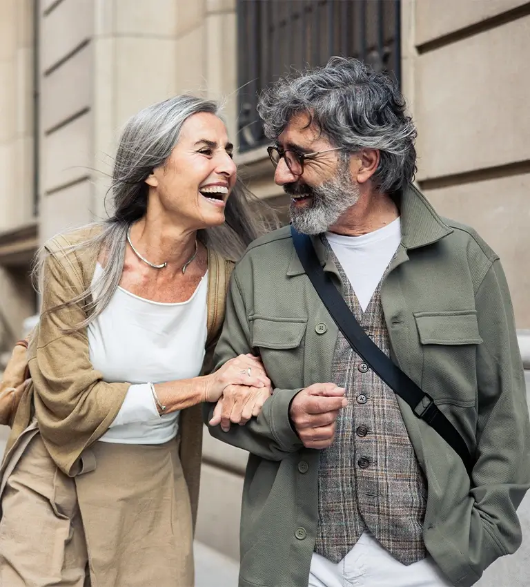 älteres Paar geht Arm in Arm die Straße entlang und lacht